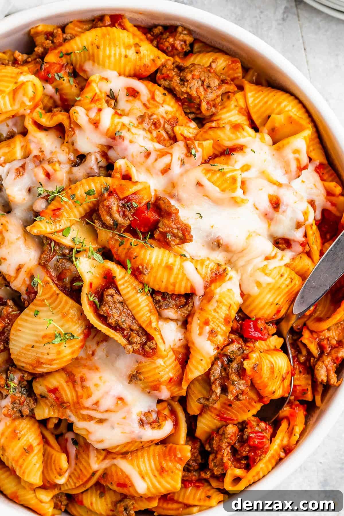 A serving dish filled with cooked pasta shells and ground beef in tomato sauce, topped with melted mozzarella.