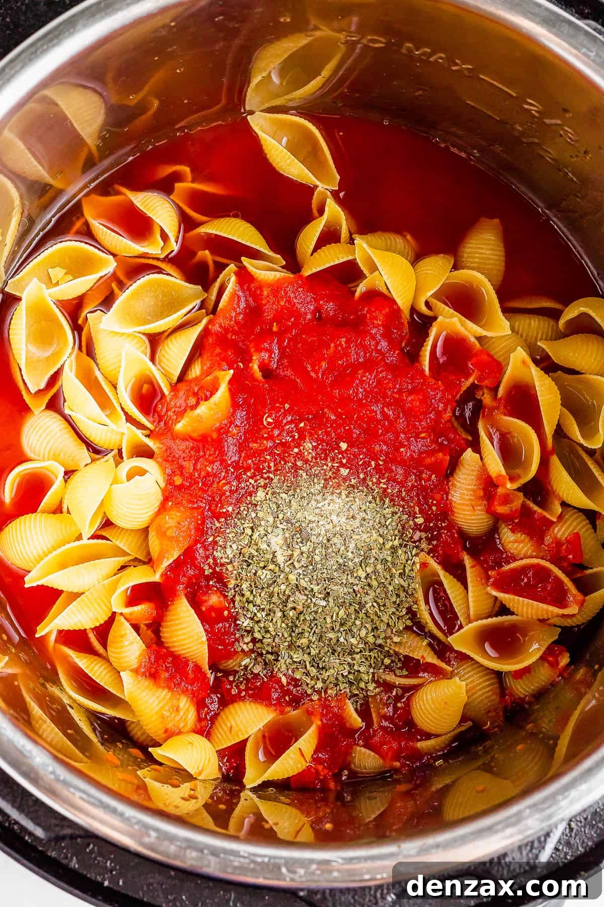 An overhead shot of an Instant Pot with crushed tomatoes, water, pasta, and seasonings inside.