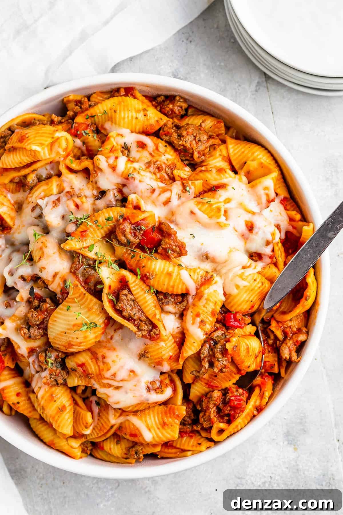A serving dish filled with cooked pasta shells and ground beef in tomato sauce, topped with melted mozzarella.