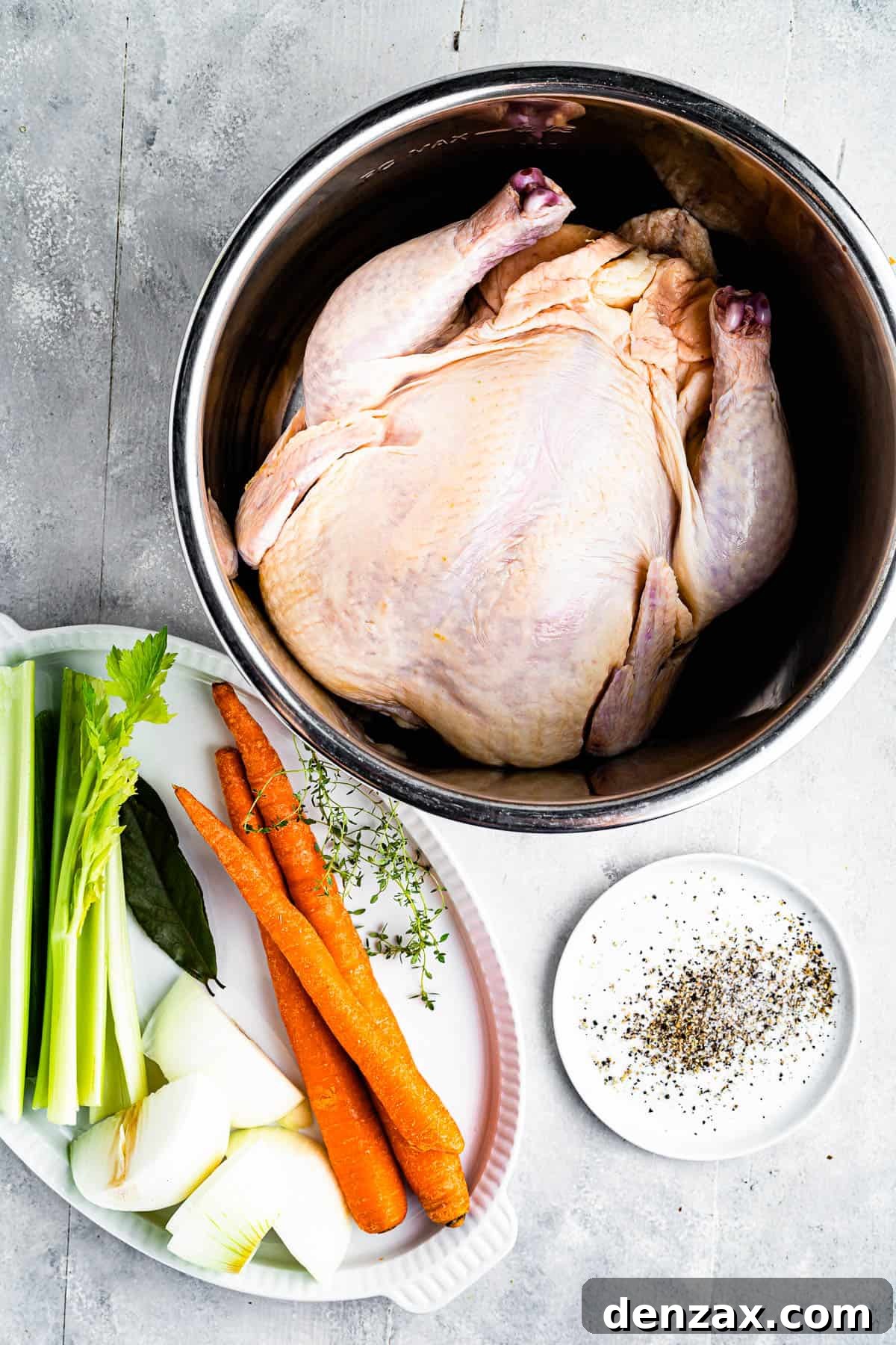Clockwise from top: a whole chicken in a pot, seasonings, and a tray of raw vegetables including carrots, onions, and celery.
