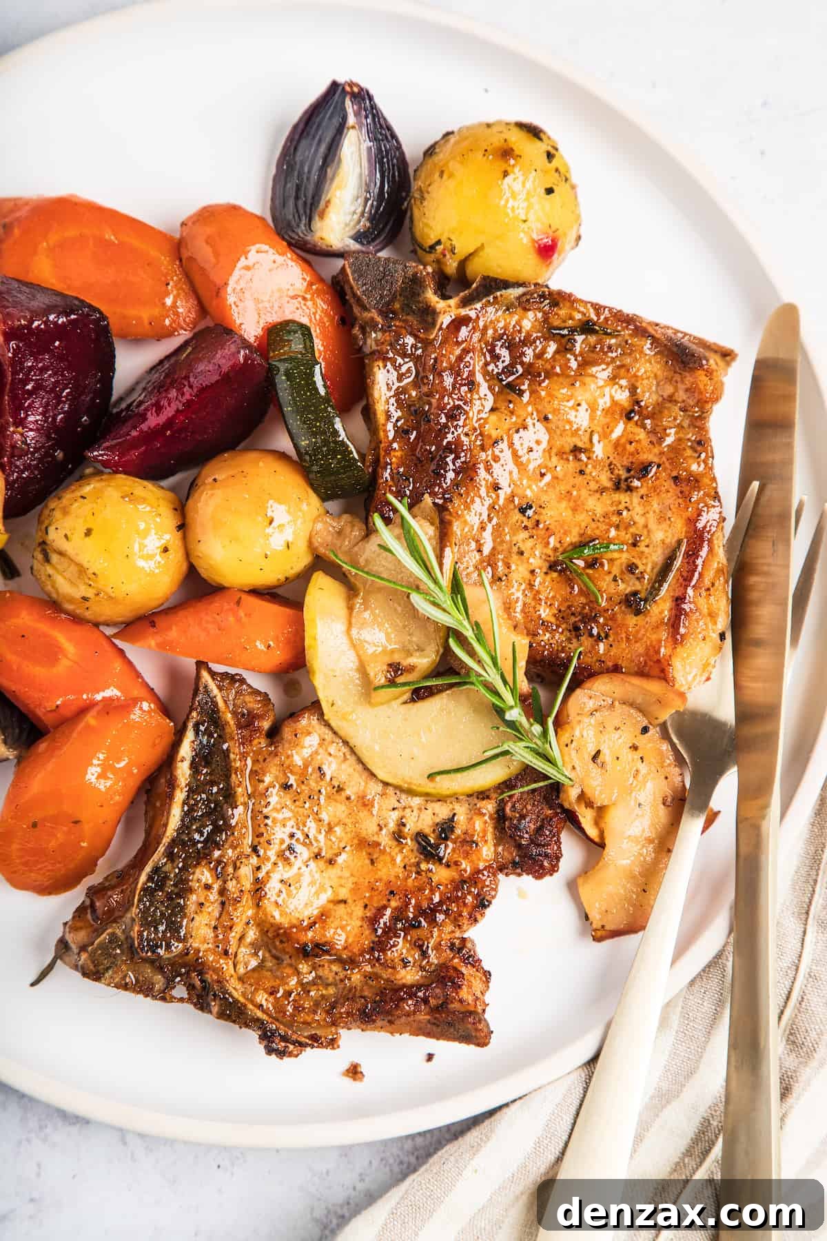 Roasted Pork Chops with Apples and Winter Vegetables 2 A plate of baked pork chops with apples and winter vegetables, garnished with a sprig of rosemary.