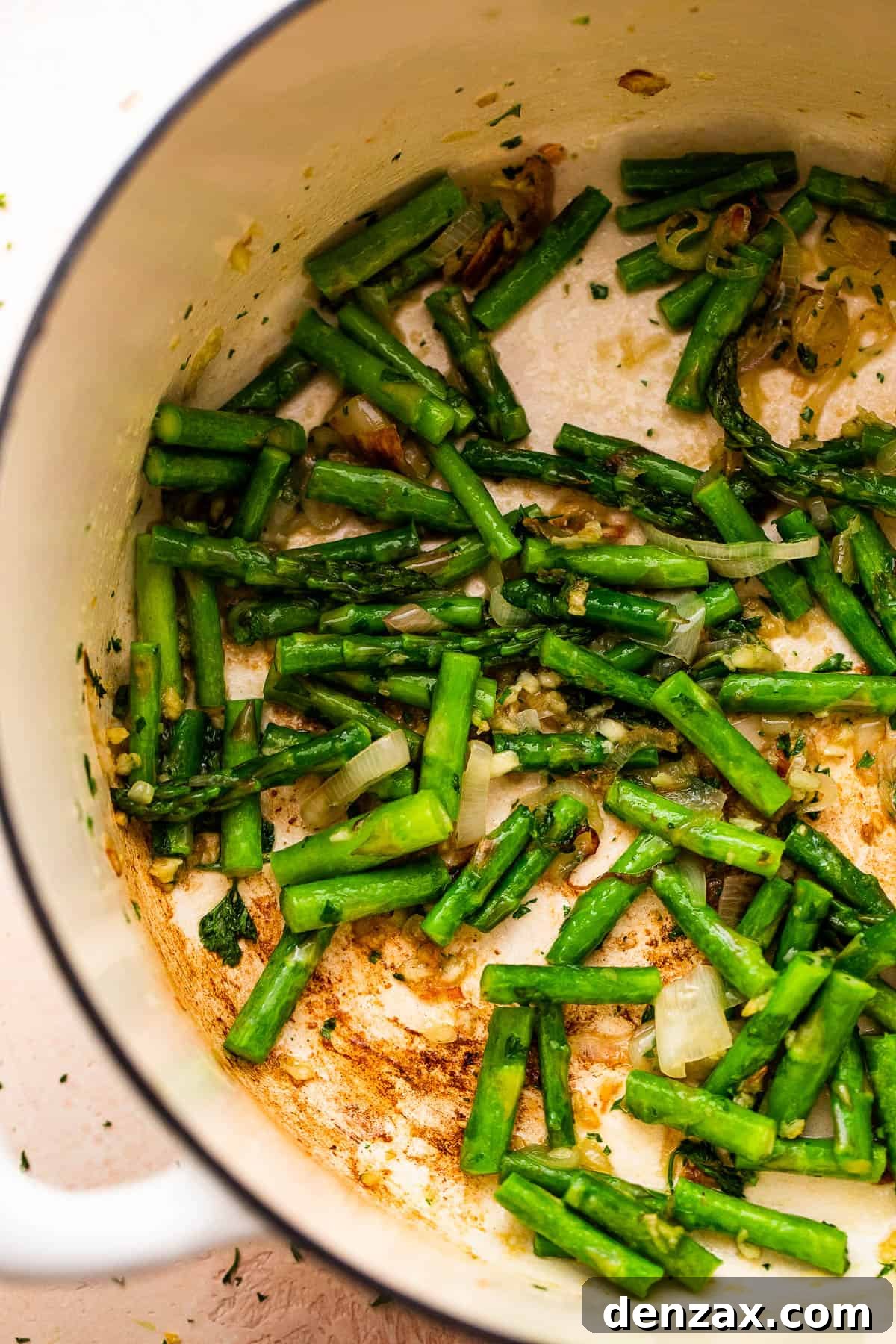 sauteeing asparagus spears inside a white dutch oven.