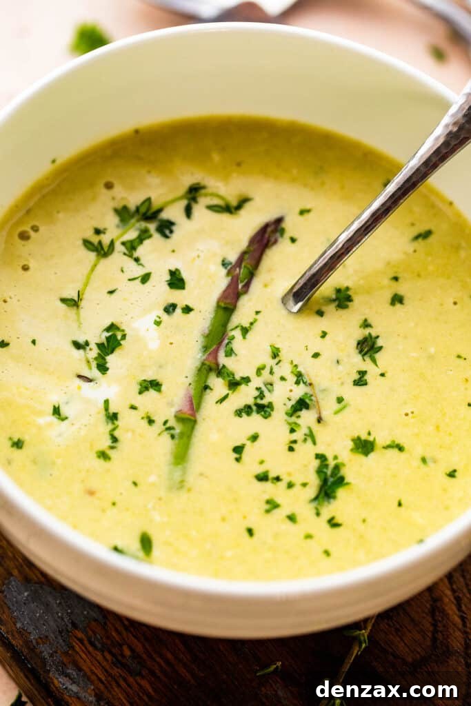 Cream of Asparagus Soup in a white bowl with a spoon inside.