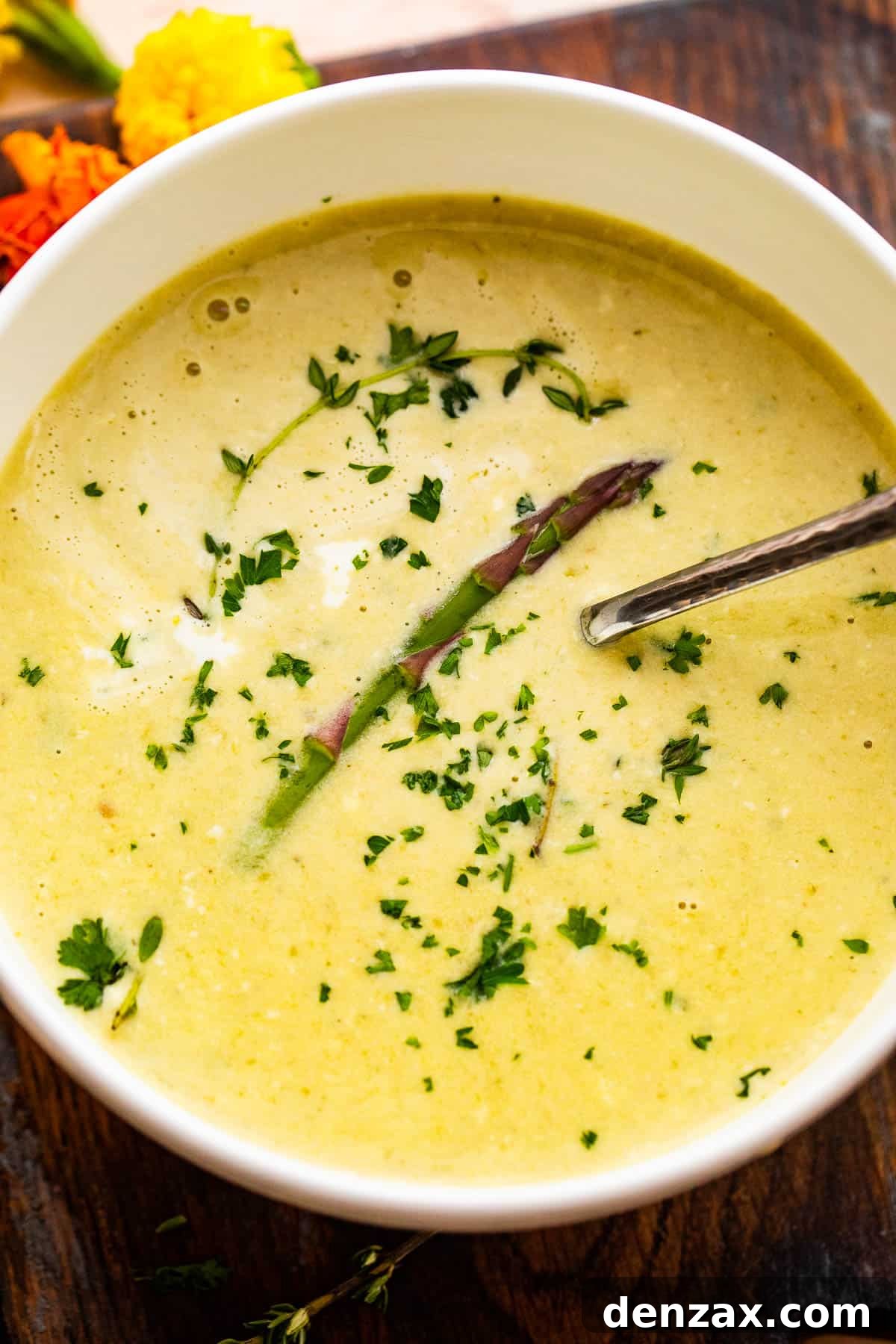 Overhead shot of Cream of Asparagus Soup served in a white bowl garnished with an asparagus spear and parsley.