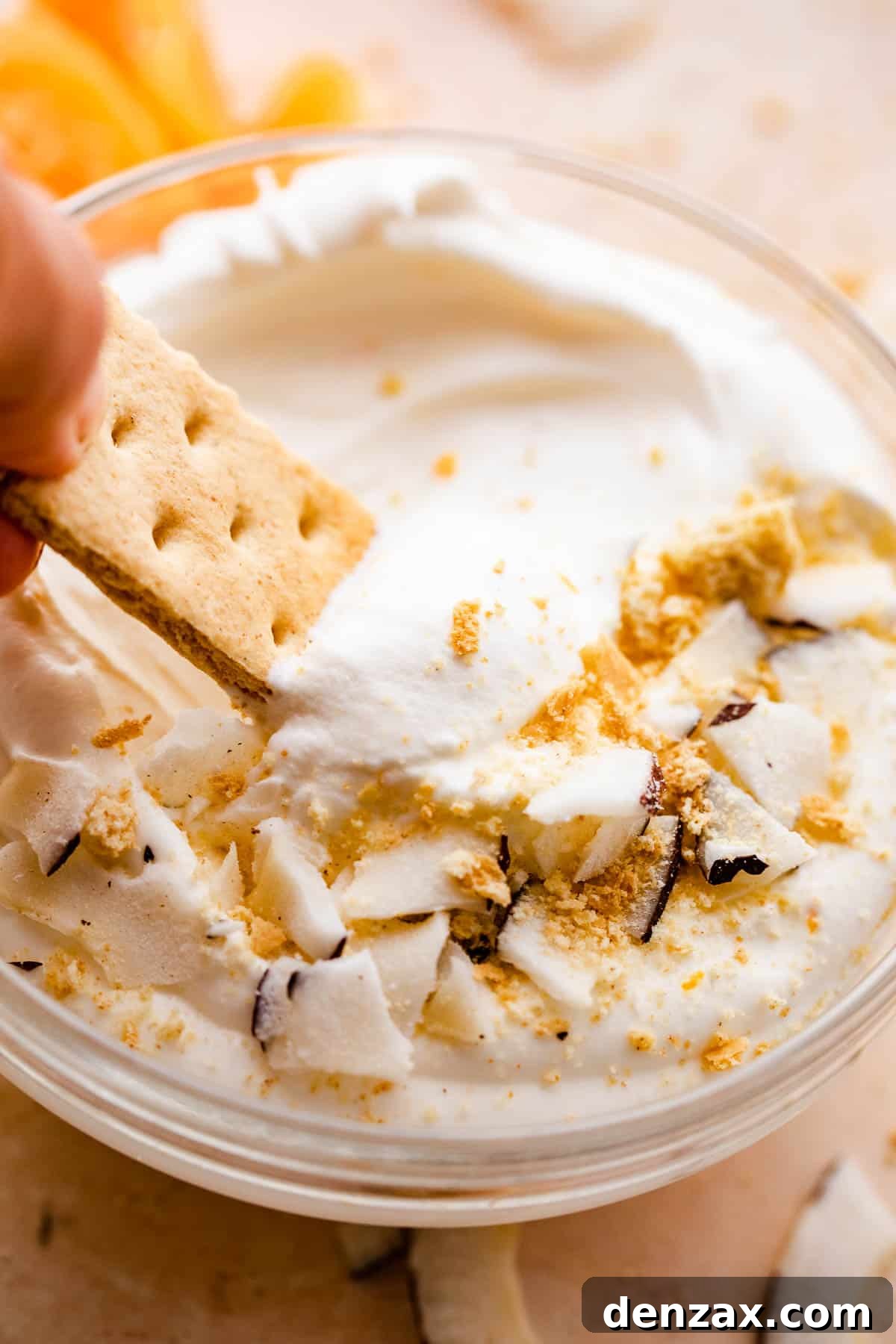 graham cracker dipping into a creamy coconut fruit dip topped with cookie crumbs and coconut shavings.