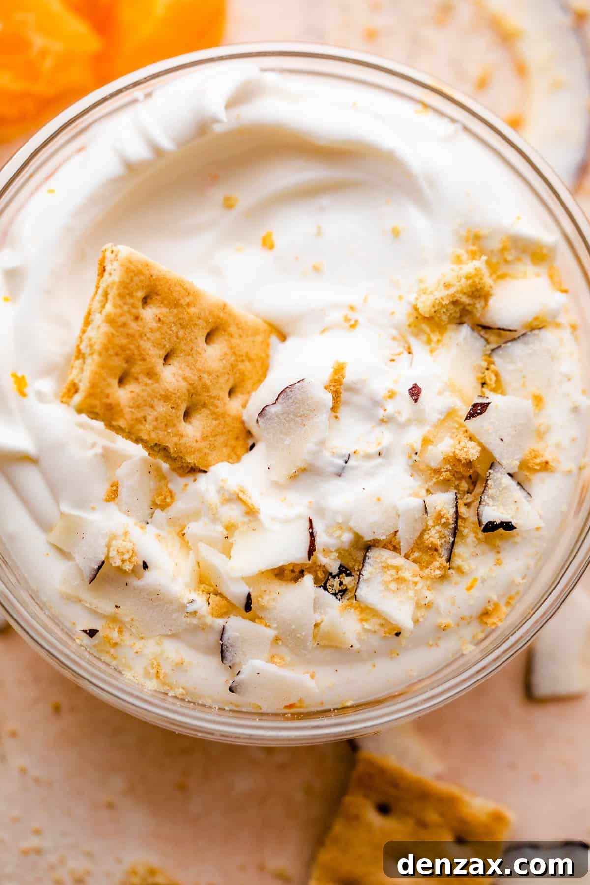 overhead shot of a creamy coconut dip served in a glass bowl with tangerine slices and coconut shavings placed around and on the sides of the bowl.