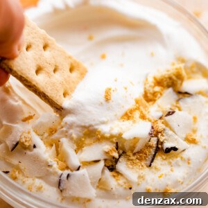 graham cracker dipping into a creamy coconut fruit dip topped with cookie crumbs and coconut shavings.