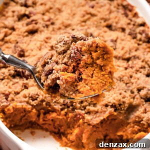 A shot of the sweet potato casserole with a serving spoon lifting a portion out of the dish, showing the texture of the baked casserole mixture and crumb topping.