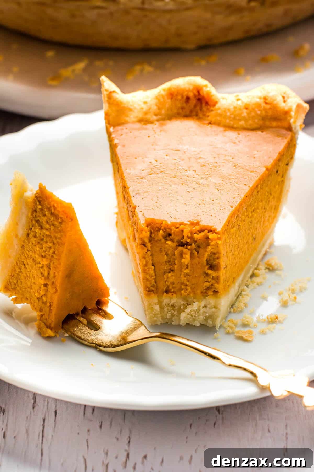 This homemade and easy Pumpkin Pie recipe is a holiday favorite! Everyone will love the tender pie crust, warm spices, and dulce de leche pumpkin filling. A pumpkin pie slice on a white plate with a fork.