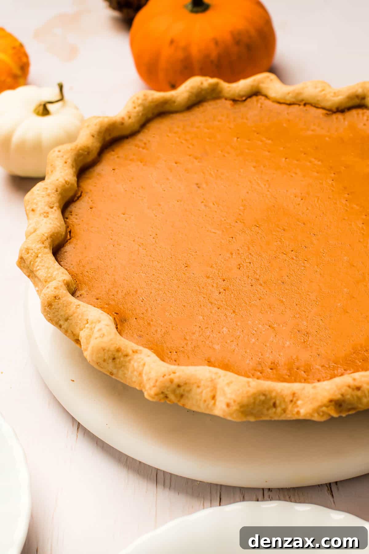 This homemade and easy Pumpkin Pie recipe is a holiday favorite! Everyone will love the tender pie crust, warm spices, and dulce de leche pumpkin filling. A baked pumpkin pie with a crimped crust on a white serving plate.
