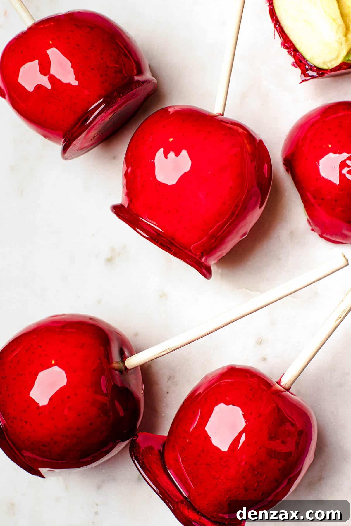 Several candy apples on a white cutting board. Plain Granny Smith apples and an orange fringed placemat in the background.