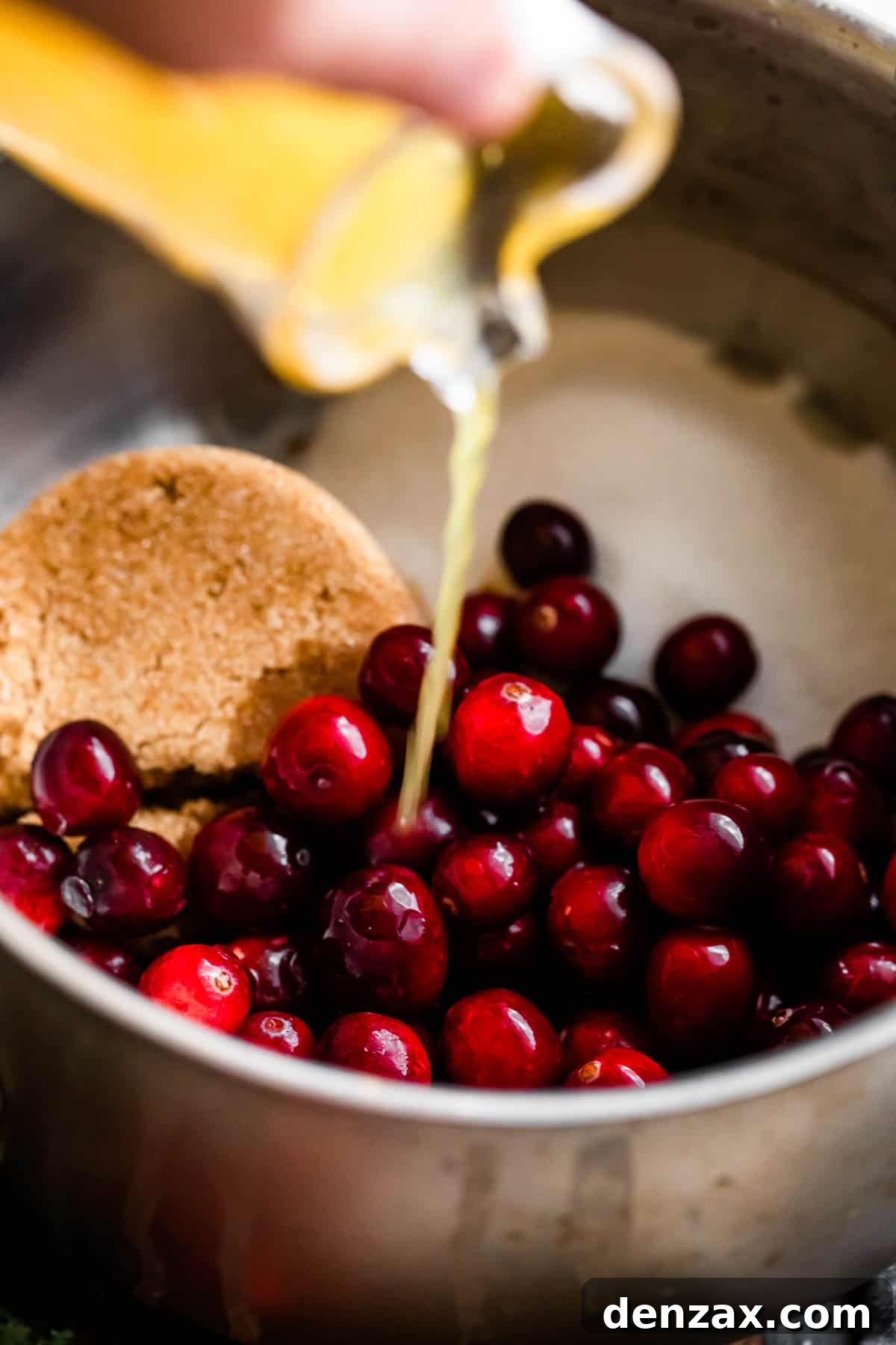 pouring orange juice over fresh cranberries and sugars inside of a saucepan.