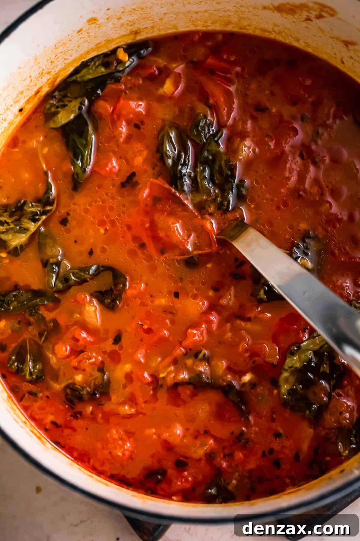 overhead shot of a pot with tomato soup and basil leaves.