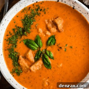 overhead shot of white bowl with tomato basil soup, garnished with croutons, parsley, and basil leaves.
