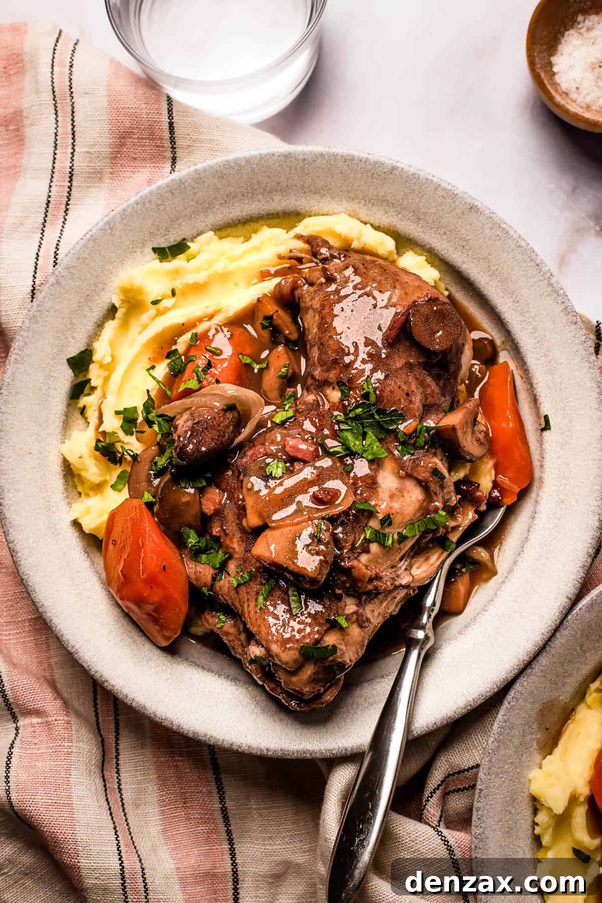 A serving of coq au vin with mashed potatoes on a stoneware plate.