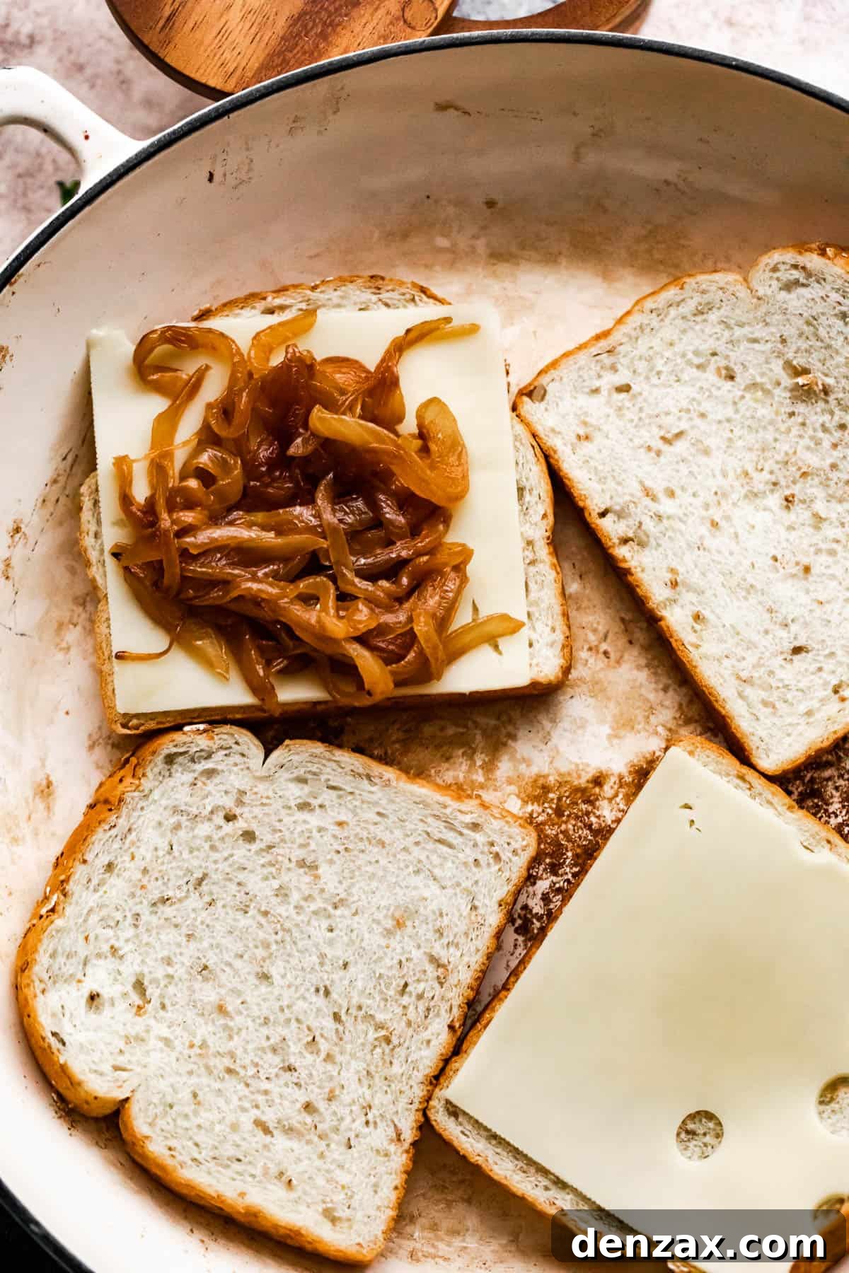 four bread slices in a skillet, with two of the bread slices topped with slices of cheese and one bread slice is topped with caramelized onions.